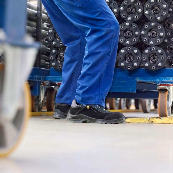 Ein junger Mann in Arbeitskleidung schiebt einen Lastenwagen vor sich her. Er achtet auf seine Haltung und trägt Arbeitsschuhe. Die Arbeitsschuhe schützen die Füße vor Verletzungen.