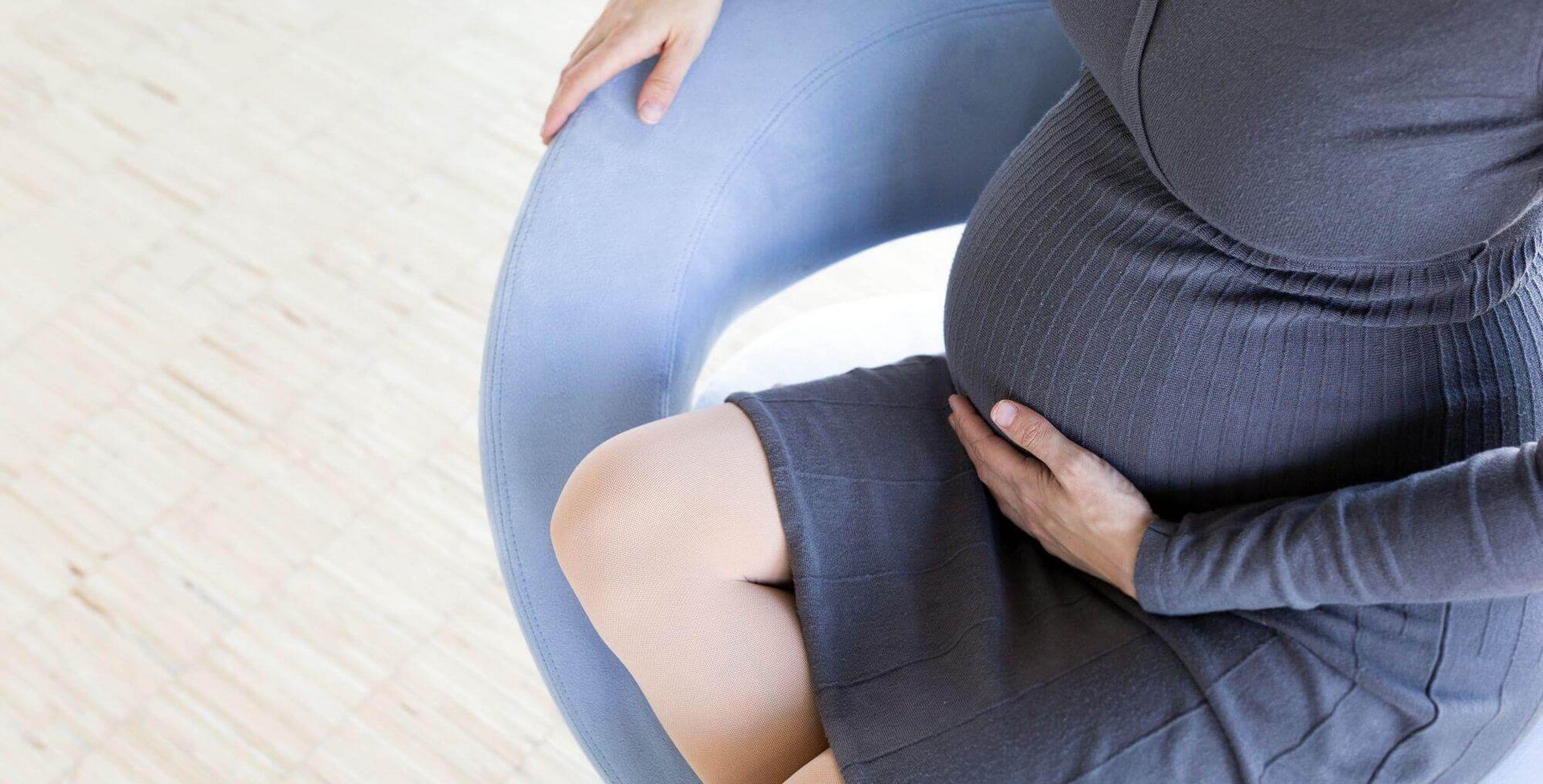 Eine schwangere Frau sitzt auf einem Stuhl und streichelt mit der linken Hand über ihren Babybauch. Besonders häufig sind Schwangere durch die enorme Veränderung und Belastung des Körpers von einer Beckenringinstabilität betroffen.