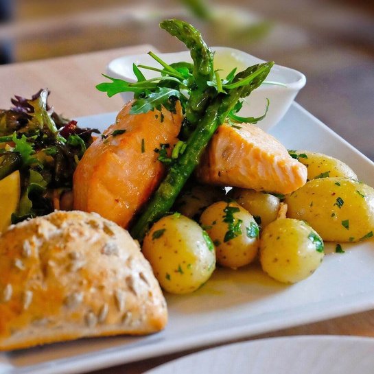 Das Bild zeigt einen Teller mit Lachs, Kartoffeln, einem Brötchen und Gemüsebeilage. Die Ernährungsweise spielt bei einer Arthrose eine wichtige Rolle.