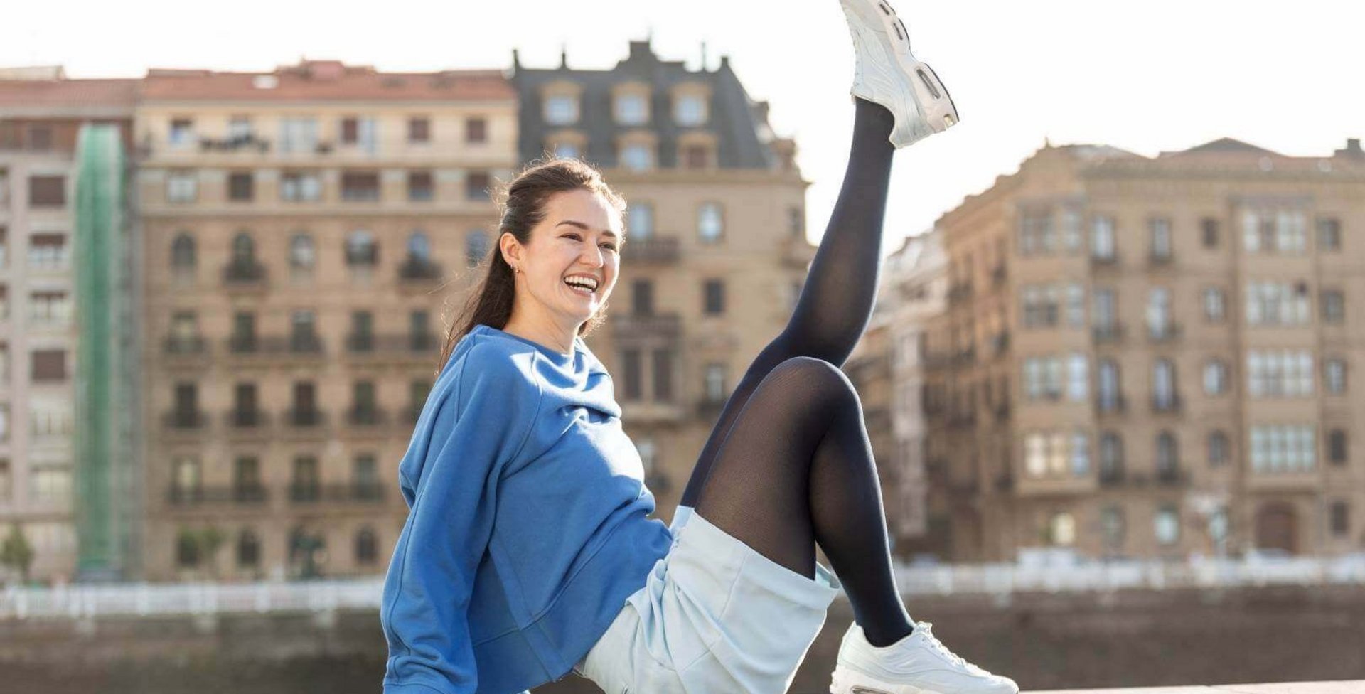 Eine Frau, die auf einer Steinmauer sitzt. Sie streckt dabei ein Bein nach oben. Sie trägt Kompressionsstrümpfe von Bauerfeind.