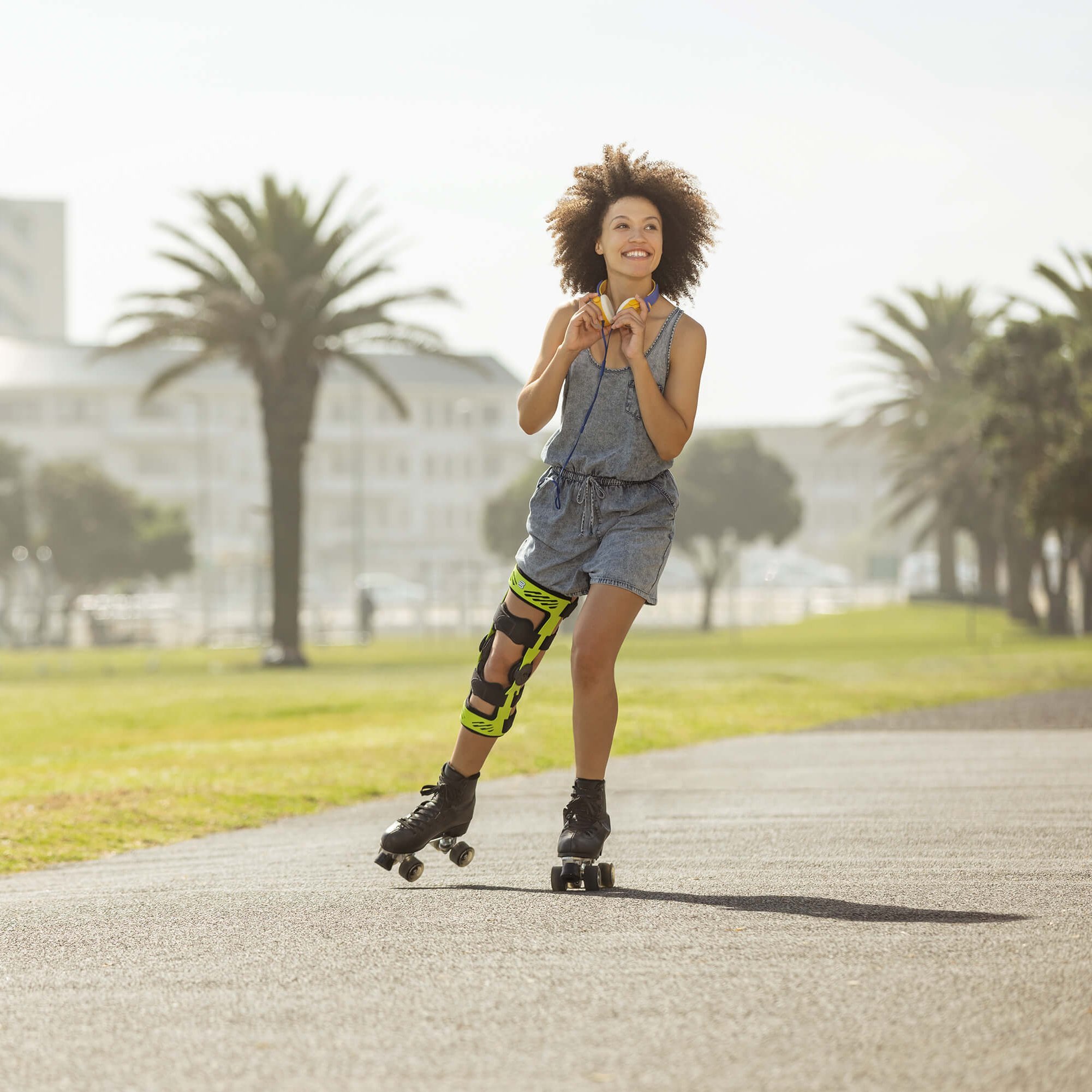 Das Bild zeigt eine lächelnde, junge Frau mit Rollschuhen an einer Strandpromenade. Am Knie trägt sie eine SecuTec Genu. Die Orthese bietet u.a. Unterstützung nach einer Unhappy Triad.