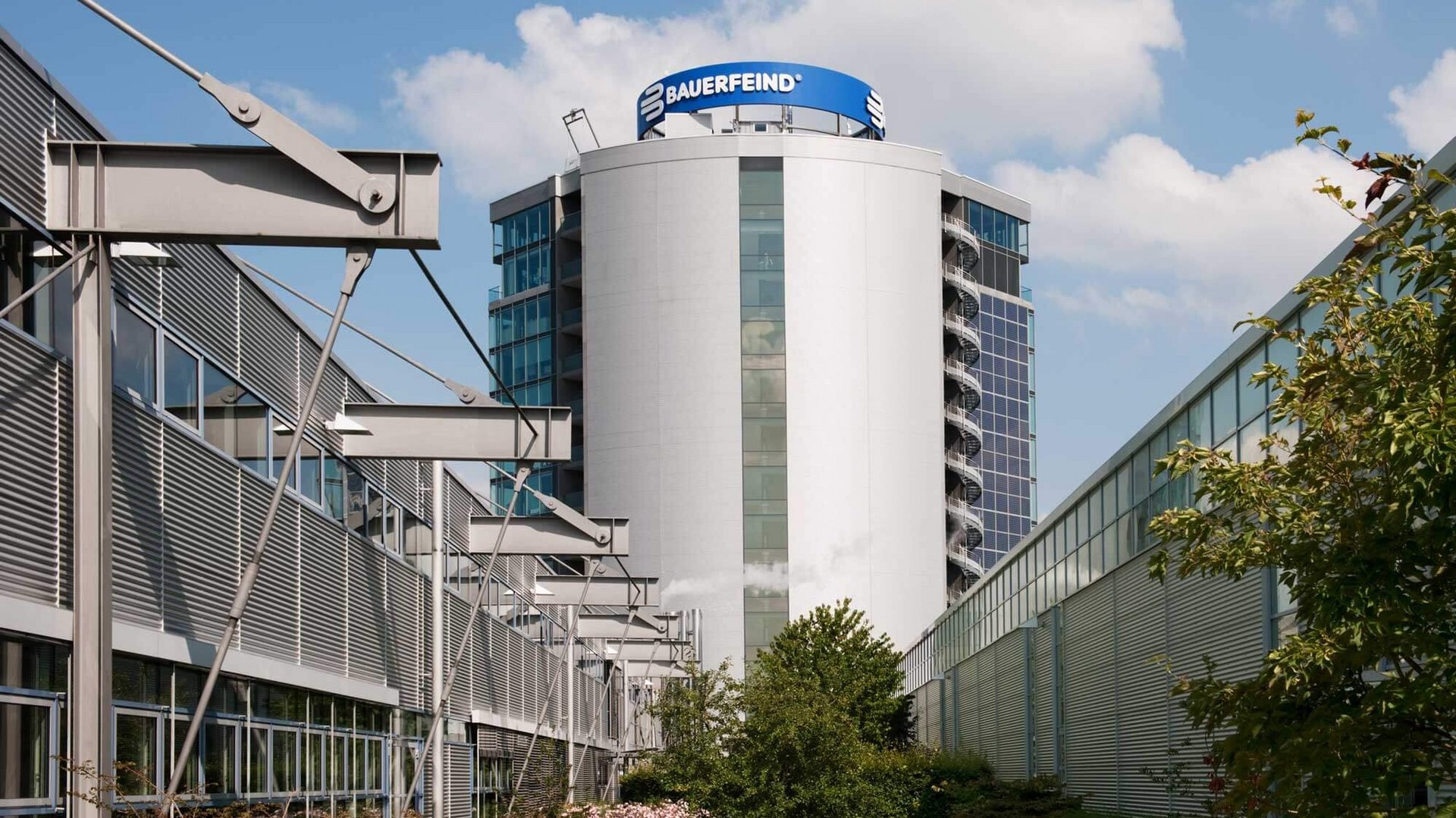 Seitenansicht des modernen Bauerfeind-Turms in Zeulenroda: Ein mehrstöckiges Gebäude mit klarer Glas- und Stahlarchitektur, umgeben von begrünten Außenanlagen.