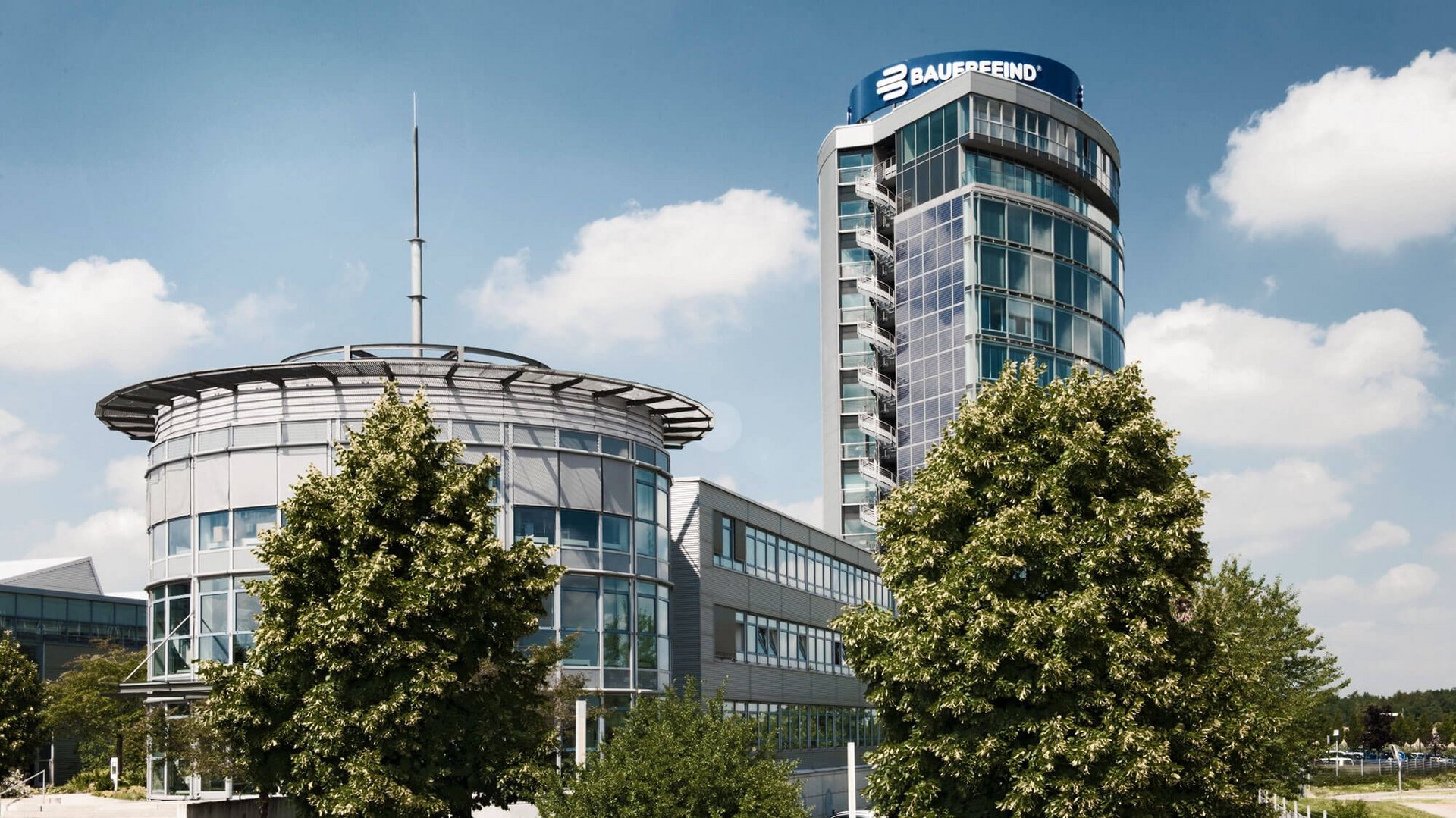 Blick auf den modernen Bauerfeind-Turm in Zeulenroda: Ein mehrstöckiges Gebäude mit klarer Glas- und Stahlarchitektur, umgeben von begrünten Außenanlagen.