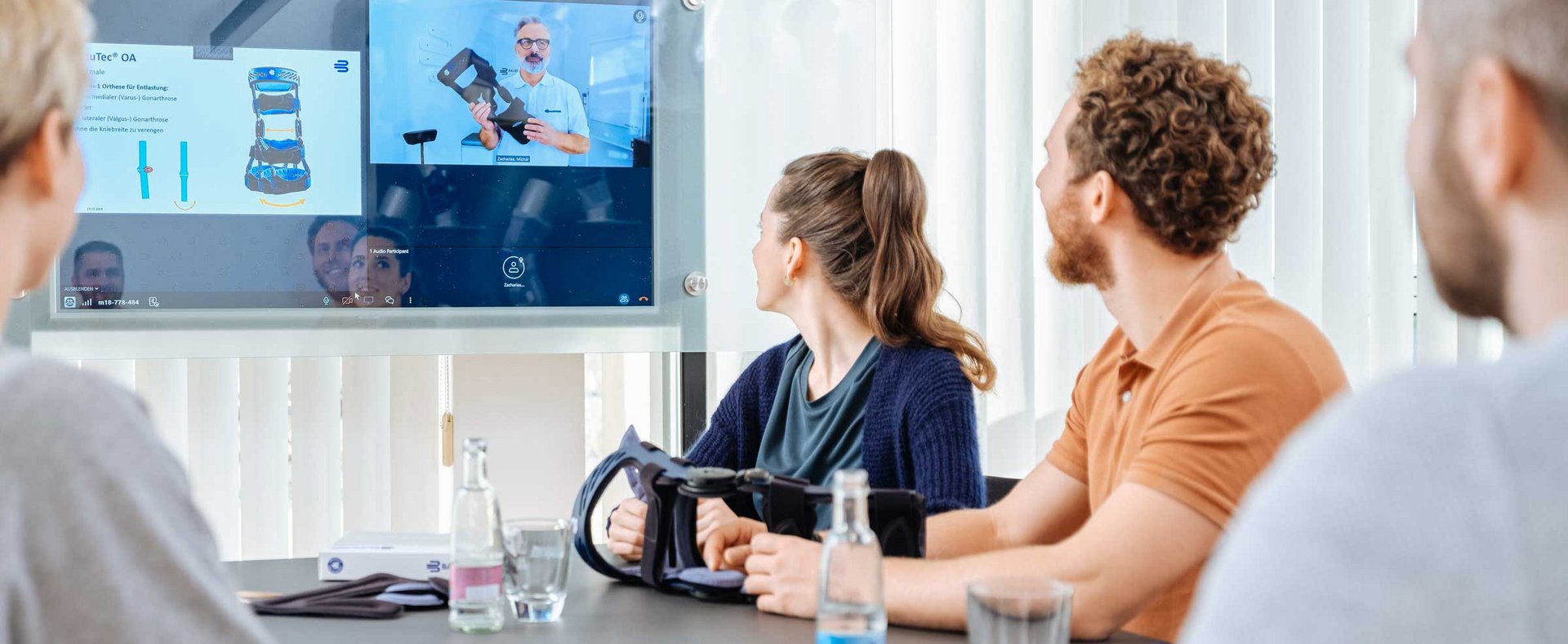 Mehrere Personen sitzen in einem Schulungs- oder Webinarraum und schauen auf eine große Projektionsfläche bzw. Leinwand, auf der Inhalte präsentiert werden. Im Vordergrund sieht man Köpfe und Schulungsteilnehmer.