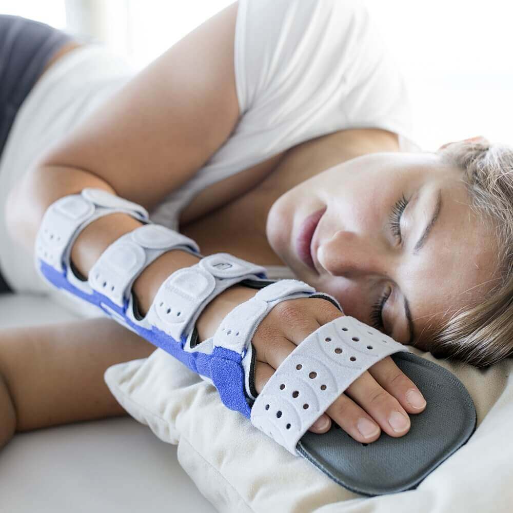 Bildausschnitt einer schlafenden Frau, die eine ManuLoc Long Plus Orthese von Bauerfeind an der rechten Hand trägt.
