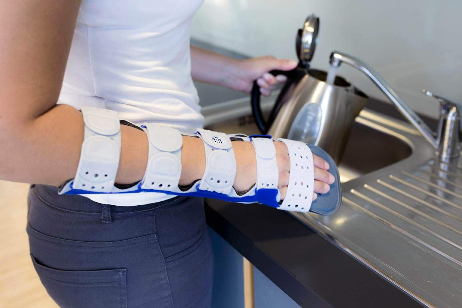 Bildausschnitt einer Frau beim Befüllen eines Wasserkochers. Am rechten Arm trägt sie eine ManuLoc Long Plus Orthese von Bauerfeind zur Ruhigstellung.